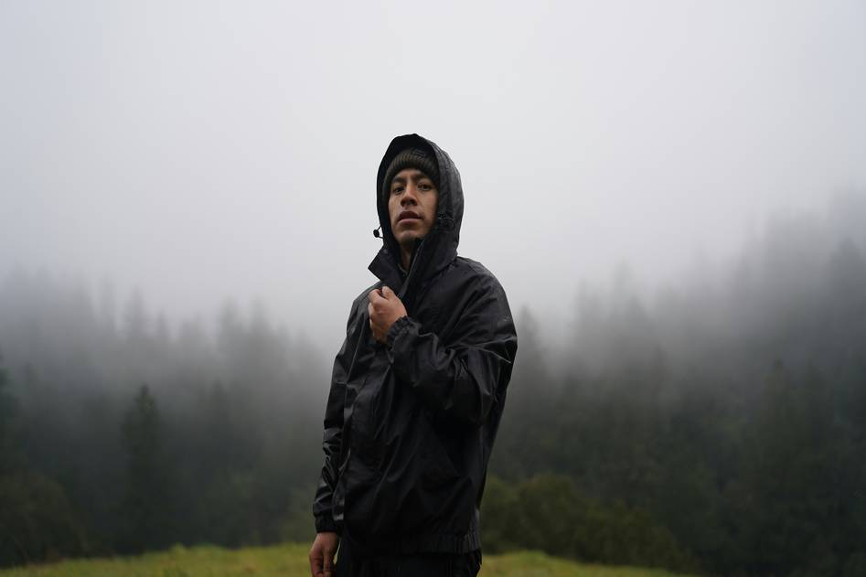 Backpacker wearing a sleek yellow rain jacket, holding a compact travel umbrella, standing confidently in light rain near a cobblestone street