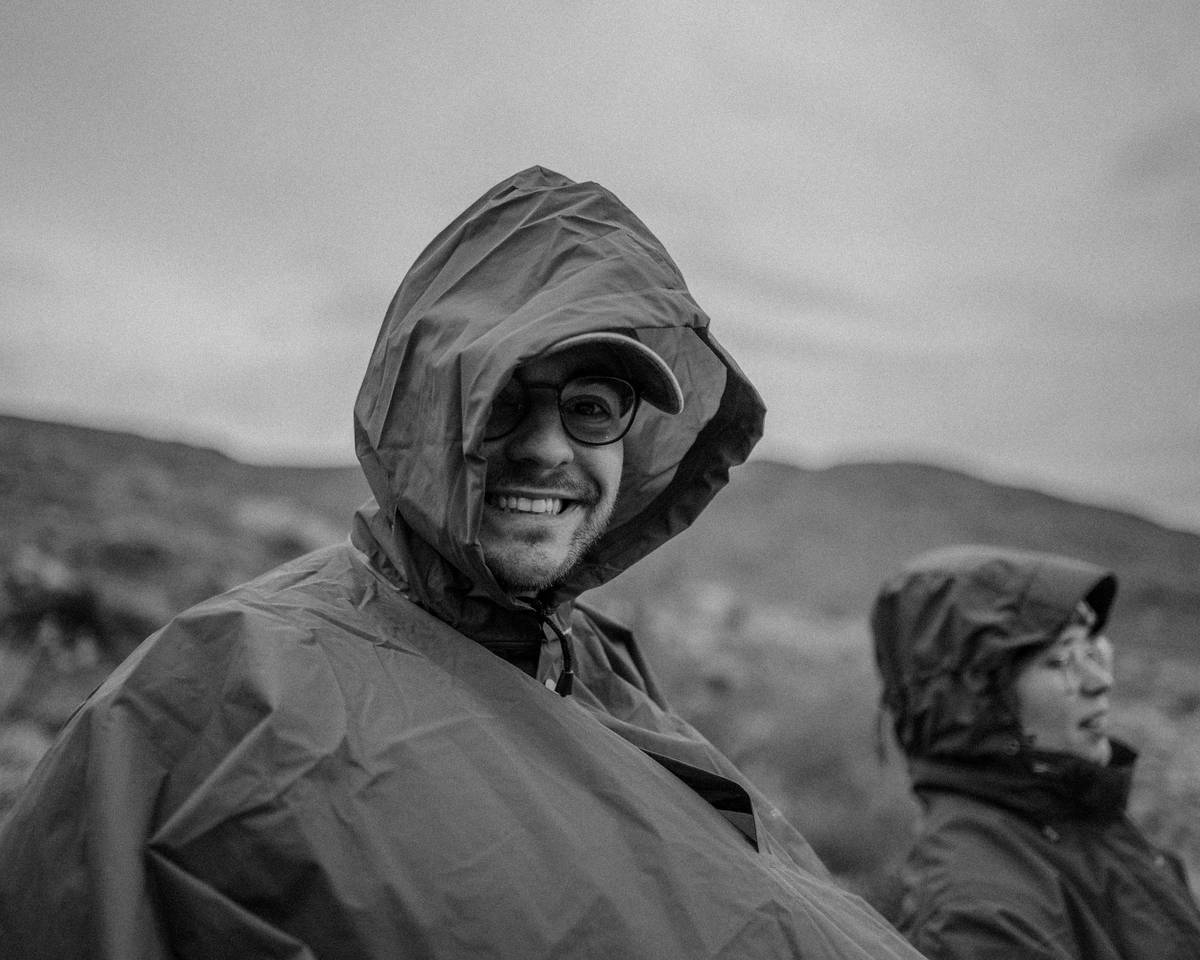 Adjustable Hoods on a black rain jacket being cinched snugly around a traveler's face in heavy rain